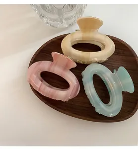 Three acetate hair claws in pink, beige, and blue shown on a dark walnut wooden tray