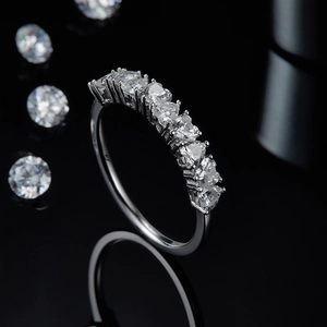 Macro detail of silver heart moissanite ring showing seven heart-cut gems on black mirror