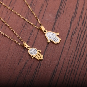 Two golden stainless steel Hamsa Hand necklaces with crystals on wooden background
