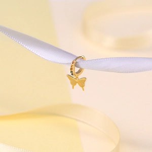 Macro detail of gold butterfly drop earring with colorful gems on a silk ribbon