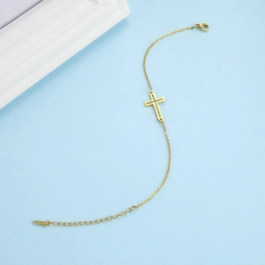 Detailed close-up of golden hollow cross charm bracelet with a slim chain and lobster clasp