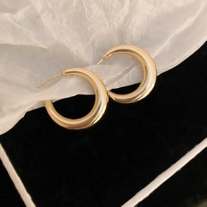 Macro view of chunky golden C-shaped metal hoop earrings on textured white paper