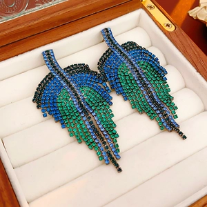Detailed view of leaf-shaped earrings with blue and green gradient rhinestones on wood box
