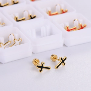 Macro shot of gold cross stud earrings with black enamel detail in a white display box