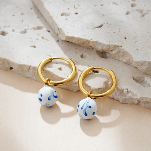 Detail of 18K gold-plated hoop earrings with blue and white porcelain charms on stone