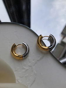Close-up of two-tone gold and silver chunky hoop earrings on a textured surface