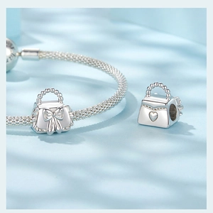 Macro detail of silver handbag charm with heart and bow motifs on snake chain