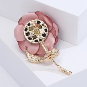 Detailed close-up of pink fabric rose brooch with golden leaves and pearl rhinestone accents