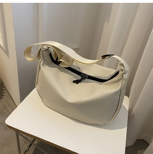 Detail view of the beige nylon crossbody bag with black dual zippers on a white table