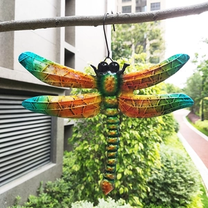 Close-up of colorful metal dragonfly wall decor hanging on a tree branch outdoors