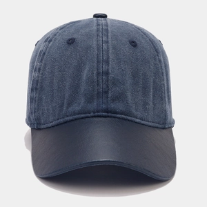Detail of grey-blue denim baseball cap with navy faux leather brim and contrast texture