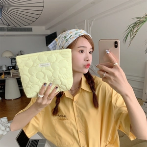 Handheld view of a large yellow floral quilted cosmetic bag with soft puffy texture
