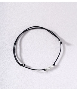 Detail of minimalist black cord bracelet with adjustable silver rings on white background
