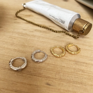 Close-up of irregular textured hoop earrings in gold and silver on a wooden surface