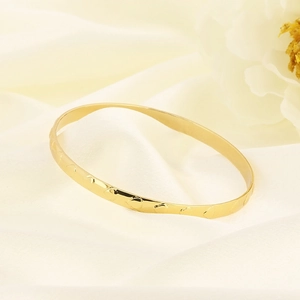 Detail of a gold titanium bangle with wave patterns on soft silk and white flower