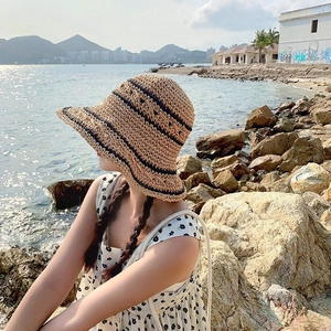 Detail of hand-woven straw hat with black stripes texture against a scenic coastal background