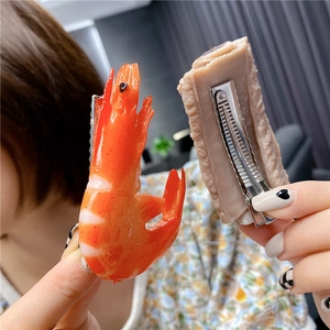 Creative shrimp and meat shaped hair clips held by hand with a blurred background