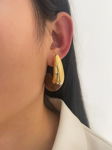 Detail of 18K gold teardrop earring with dark brown resin inlay on a female model