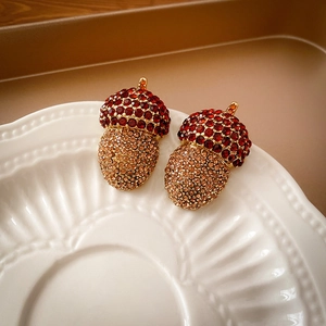 Macro detail of acorn charm with deep red and champagne crystals on ceramic plate