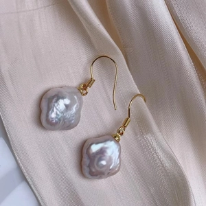 Macro shot of baroque pink-purple pearl earrings with golden hooks on silk background