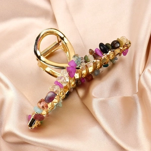 Detail view of large gold claw clip with colorful natural crystal stones on satin fabric