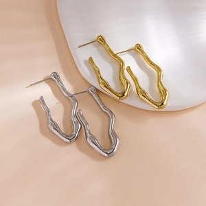 Detailed view of wavy C-shape earrings in gold and silver finish on a white stand