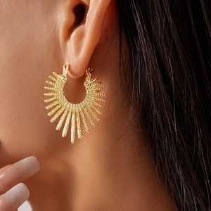 Close-up of a gold-toned sunburst fan earring worn on model featuring metal texture