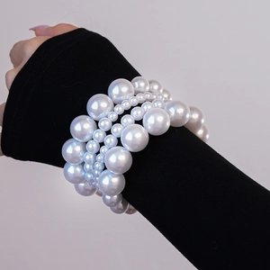 Détail de bracelets en perles blanches multicouches de tailles variées sur manche