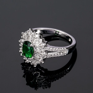 Silver ring with oval green emerald and diamond flower halo on black reflective surface