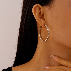Detail of silver chain link hoop earrings on model highlighting metallic texture