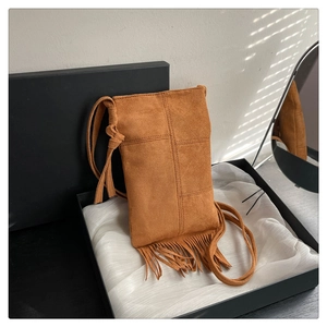 Detail of a brown suede bohemian tassel crossbody bag on a silk background