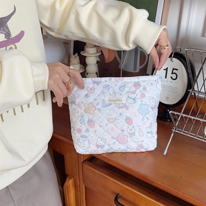 Detailed view of cream quilted makeup bag with pastel cartoon prints held by hand