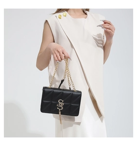 Close-up of black quilted shoulder bag with gold S-logo and fringe metal chain strap