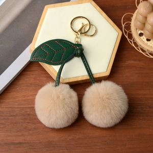 Detail of faux rabbit fur cherry keychain with soft cream pom-poms on a wooden tray