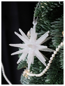 Macro shot of white sparkling star ornament with glitter on a green Christmas tree branch