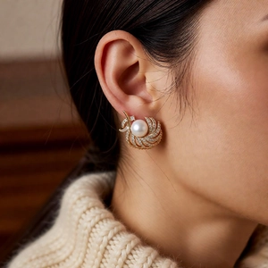 Detail of 18k gold plated earring with white pearl and feather-shaped diamonds on a model