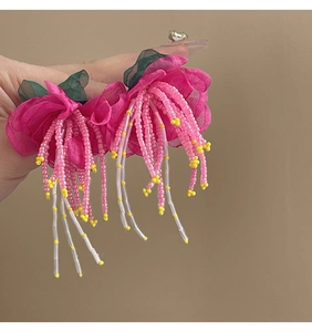 Detail of fuchsia fabric flower earring with beaded tassels held against a brown wall