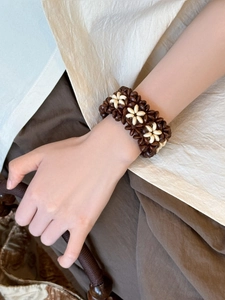 Detail of bohemian wood bead bracelet with white flower charms on a model's wrist