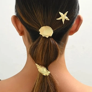 Detailed view of three gold starfish, shell, and conch hair accessories on a bubble braid
