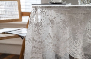 Detailed close-up of white lace tablecloth featuring floral embroidery and wavy edges