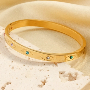 Golden evil eye bangle with colorful rhinestones on a white stone stand with satin backdrop