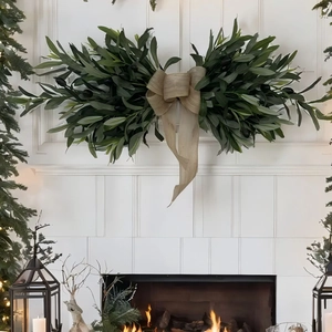 Close-up of olive leaf wreath with large burlap bow against a cozy fireplace background