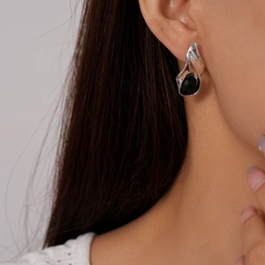 Macro shot of silver teardrop earring with black stone on ear of female model