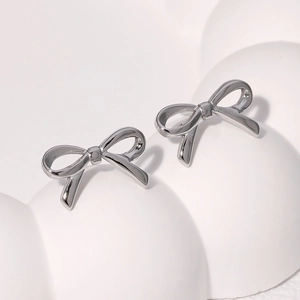 Detail view of silver bow-shaped stud earrings on a white minimalist background