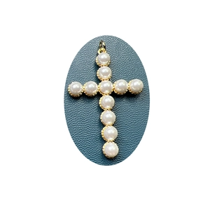Elegant gold cross pendant with white pearls on a dark textured background display