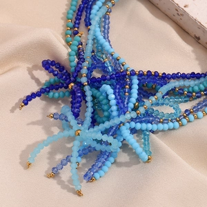 Detail of handmade blue layered beaded necklace with gold accents on silk fabric