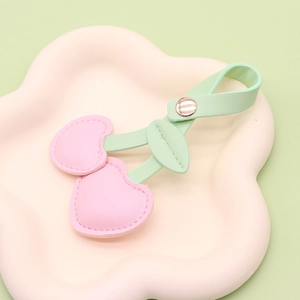 Pastel pink cherry leather keychain with green leaves and gold snap button on a tray