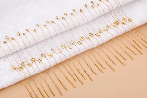 Detail of gold letter necklaces A-Z with zircon inlay on a white fur and beige background
