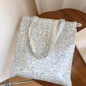 Détail d'un sac cabas en toile à fleurs lavande posé sur une surface en bois rustique