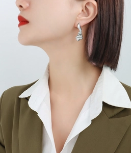 Détail macro de la boucle d'oreille ondulée en métal argenté portée par un mannequin